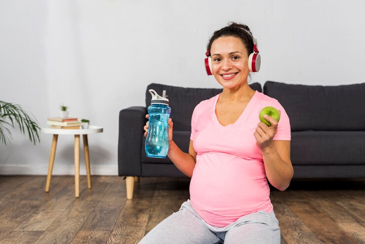 embarazada bebiendo agua con manzana verde en mano